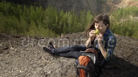 一个旅游女孩坐在山上在夏天吃一个绿色的苹果视频的预览图
