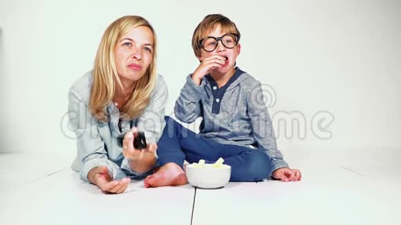 母亲和儿子躺在地上吃薯片看电视视频的预览图
