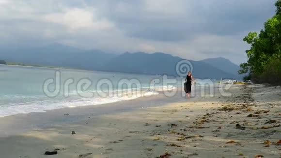 一个穿着漂亮黑色裙子的女孩在海边散步和跑步视频的预览图