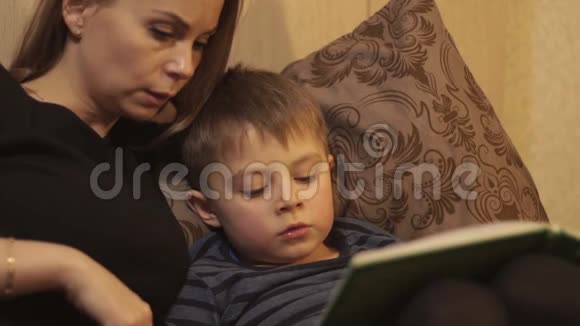 年轻的母亲和小儿子在舒适的卧室里躺在床上看书视频的预览图