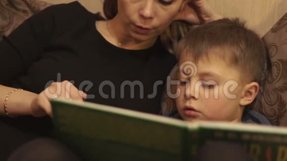 年轻的母亲和小儿子在舒适的卧室里躺在床上看书视频的预览图