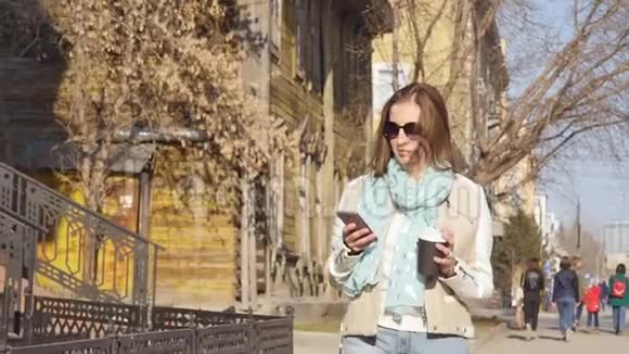 年轻的商务女性在街上散步午餐休息时喝咖啡使用智能手机视频的预览图