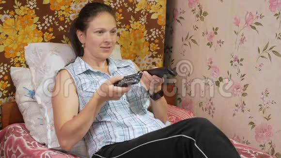 年轻女子躺在家里的沙发上穿着电视里的外套聚精会神地看着屏幕视频的预览图