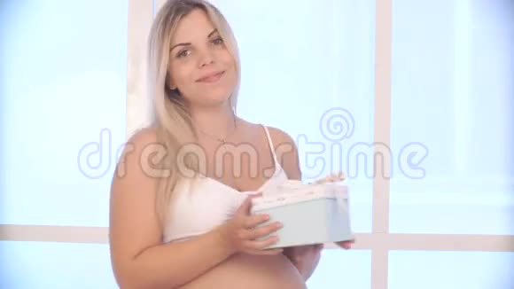 孕妇为礼物感到高兴金发女郎打开一个带礼物的盒子视频的预览图
