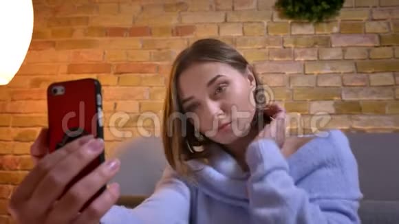 年轻白种人可爱的女性在手机上自拍并在镜头前摆姿势的特写照片视频的预览图