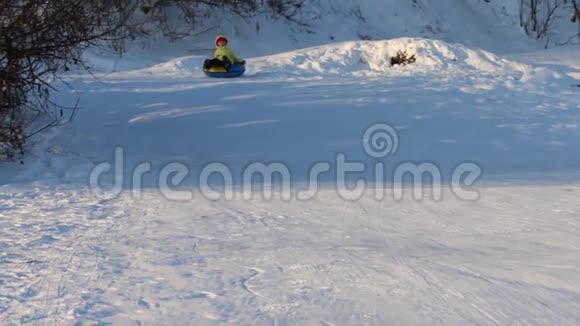 阳光明媚的冬日快乐的女孩从雪筒滑下山坡视频的预览图