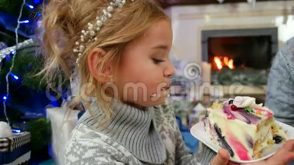 在圣诞树上高兴地吃着一大块蛋糕的女孩一家人在壁炉旁吃着带茶的甜点视频的预览图