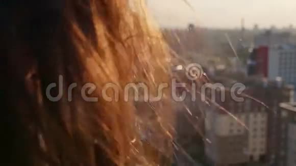 后景特写风吹着长长的黑发美丽的年轻女人日落时站在屋顶上的女孩慢节奏视频的预览图