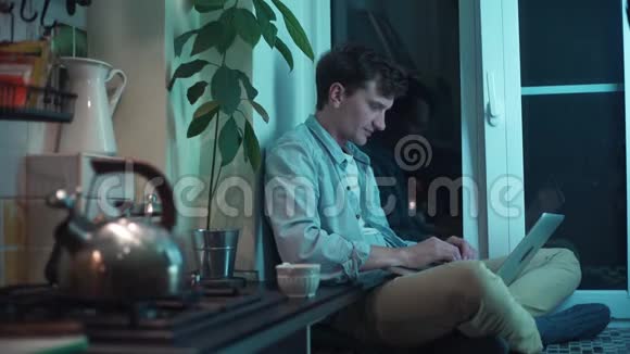 年轻人坐在厨房里打电脑一边烧水壶视频的预览图