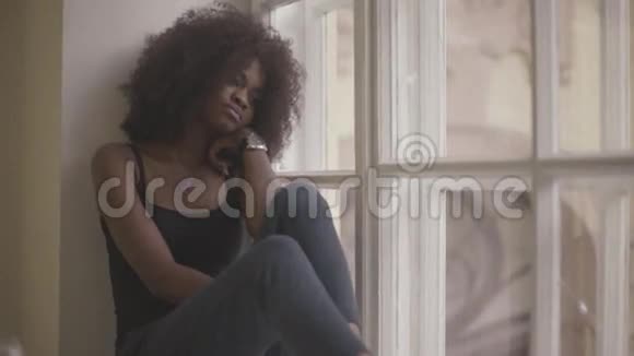 美丽而悲伤的年轻非洲女人坐在窗台上悲伤视频的预览图