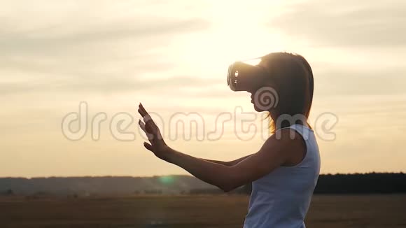 日落时在野外的虚拟现实护目镜中的女孩女人看着太阳的虚拟现实眼镜视频的预览图
