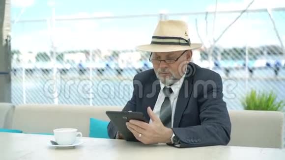 友好的英俊老人在咖啡馆里带着平板电脑4K视频的预览图