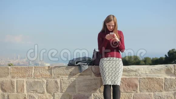 美丽的女性坐在老砖墙上用电话视频的预览图