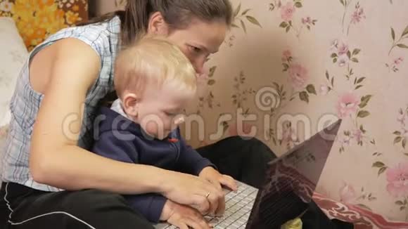 年轻女子带着儿子坐在家里的沙发上拿着笔记本电脑仔细看屏幕按下键视频的预览图