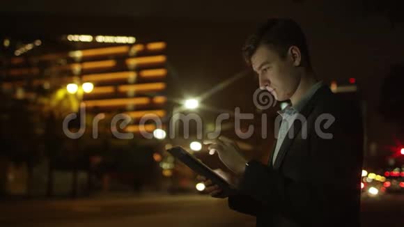 年轻人晚上在街上使用平板电脑视频的预览图