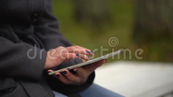 在秋天公园坐在长凳上时年轻的女人用平板电脑女性手触摸平板电脑的特写视频的预览图
