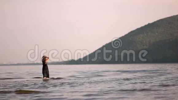 河边的女孩穿着一件黑色的衣服在群山的背景下来到水里视频的预览图