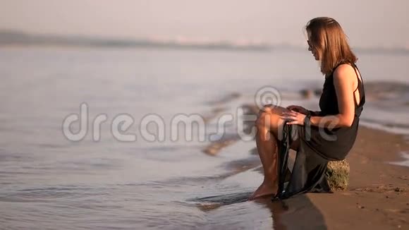 小女孩穿着黑色的衣服坐在河边的岩石上站起来在水面上行走视频的预览图