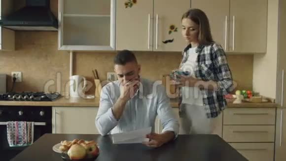 一个年轻人看着未付的账单心烦意乱被妻子抱在家里的厨房里支持他视频的预览图