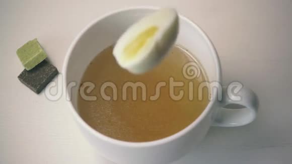 鸡蛋掉进清汤的白色杯子里慢动作视频的预览图