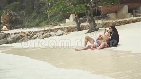 带椰子饮料的情侣在海滩上放松视频的预览图