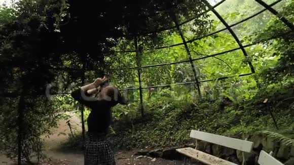 4K美丽的女孩穿着黑色手工服装站在椭圆形的夏季花园里金属乔木建筑拍摄照片视频的预览图