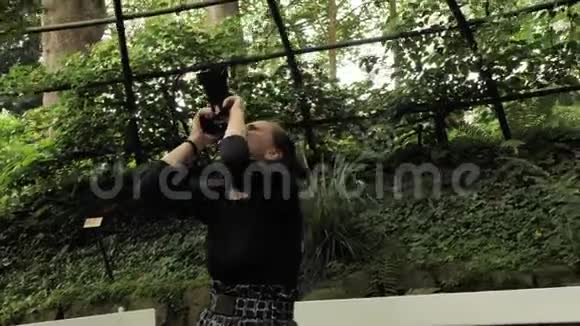 4K美丽的女孩穿着黑色手工服装站在椭圆形的夏季花园里金属乔木建筑拍摄照片视频的预览图