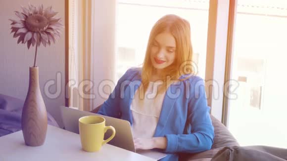 穿蓝色夹克的女孩在沙发上用笔记本电脑工作视频的预览图