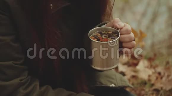 美丽幸福的年轻女子在秋林篝火旁喝热茶特写橡树叶河边女人和她在一起视频的预览图