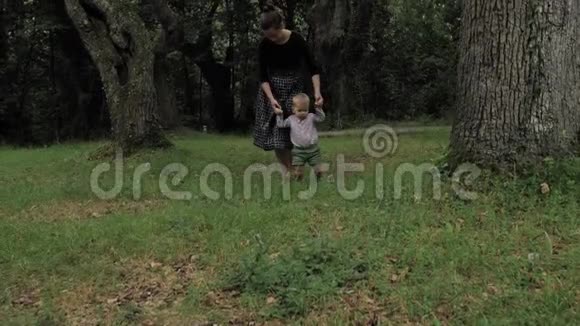 穿着黑色手工服装的漂亮女孩和她一岁的小蓝眼睛漂亮的绿色儿子一起散步玩耍视频的预览图