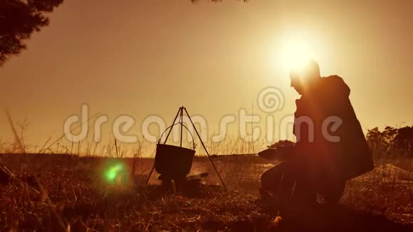 男子旅游徒步旅行者的生活方式是啤酒坐在篝火晚会上在大自然露营剪影阳光日落男人视频的预览图