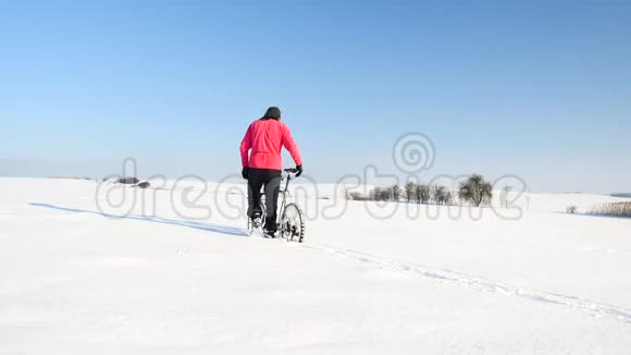 雪地上骑山地车的人骑自行车的人在大雪中推自行车冬日阳光灿烂视频的预览图