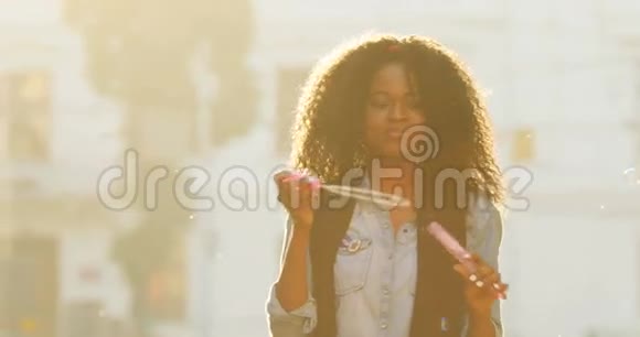 在阳光下吹肥皂泡的卷发美国黑人女孩的特写照片视频的预览图