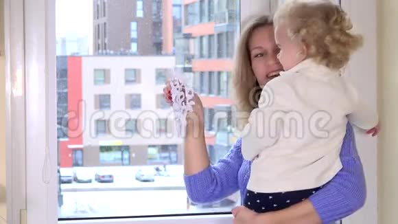快乐的母亲和她蹒跚学步的女儿女孩把纸雪花贴在窗户上视频的预览图