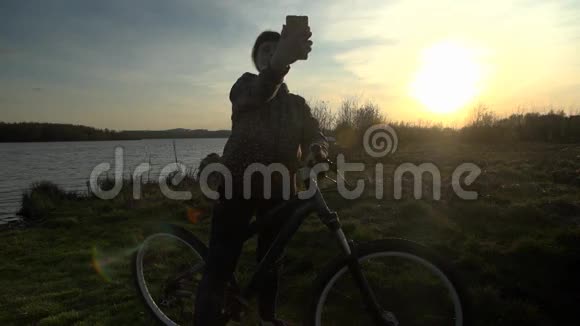 年轻女子骑自行车在日落时使用电话视频的预览图