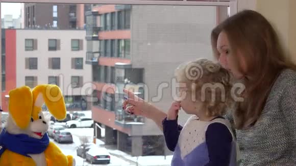 妈妈带着她蹒跚学步的女儿坐在窗户附近看到雪花视频的预览图