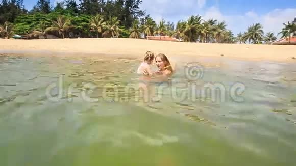 母亲在棕榈滩的蔚蓝海中高举小女孩视频的预览图