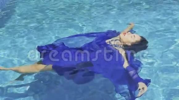 迷人的深色头发红色的嘴唇穿着蓝色的裙子在游泳池里缓慢地游泳视频的预览图