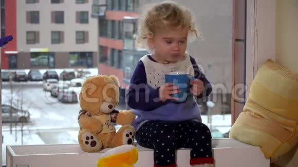 女孩坐在窗边喝着热茶看着冬天的雪花视频的预览图