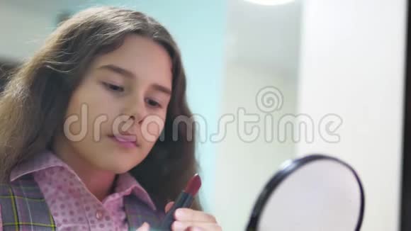 小女孩用口红涂嘴唇女学生在室内镜子前涂红唇膏视频的预览图