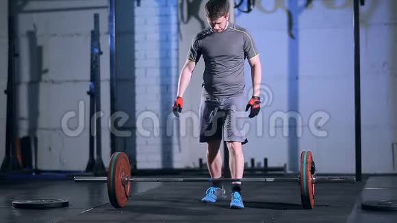 强壮的男人在健身房里用杠铃在灰色混凝土墙上做运动视频的预览图