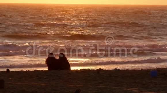 两名女性在日落时坐在沙滩上视频的预览图