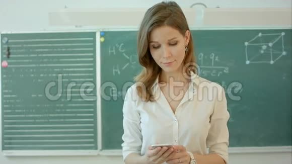 女教师或学生在黑板前教室用电话发短信视频的预览图