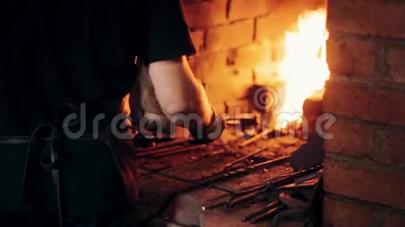 在工作场所穿围裙的铁匠人的近景用火从炉子里取出铁水视频的预览图