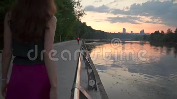 日落时分孤独美丽的黑发女孩在公园的堤岸上散步慢镜头视频的预览图