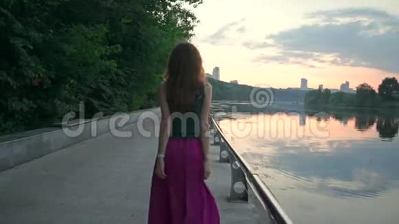 日落时分美丽的黑发女孩走在公园的堤岸上慢镜头视频的预览图
