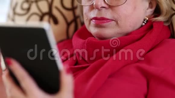 老妇人坐在沙发上用电子书女人读一本书视频的预览图