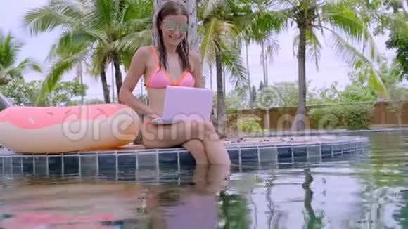 年轻的女性自由职业者坐在游泳池附近的笔记本电脑假期里很忙远程工作的概念视频的预览图