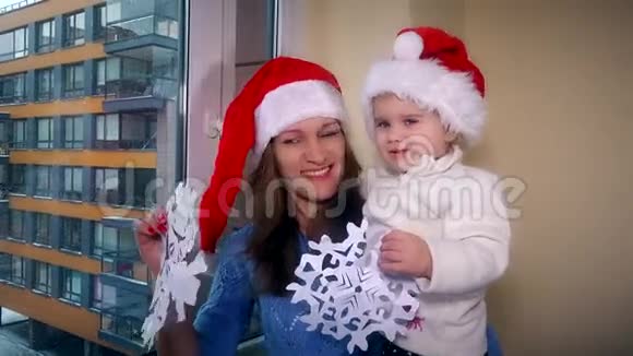 可爱的女人和孩子戴着红色圣诞帽窗户上有雪花视频的预览图