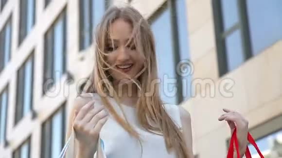 年轻的金发女孩沿着商店橱窗购物愉快视频的预览图